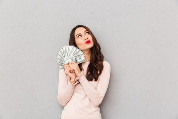 Image of lucky brunette female holding fan of 100 dollar bills being excited to win cash prize...