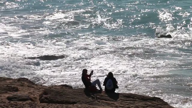 Couple of girls sitting on the edge of a cliff contemplating the strong waves