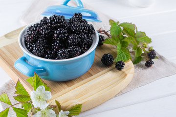 Ripe blackberries with leaves in a blue ceramic bowl on white table