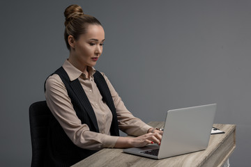 beautiful kazakh businesswoman using laptop at table isolated on grey