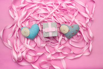 Textile heart gift against a Coil of decorative satin ribbons of pink color.