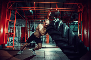 Shirtless man flipping heavy tire at crossfit gym