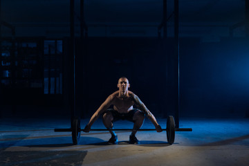 Fototapeta na wymiar A sporty man lifts a bar in the gym in a dark light
