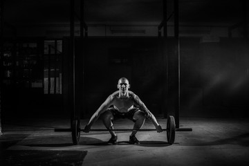 Athletic man lifts barbell in gym black and white filte