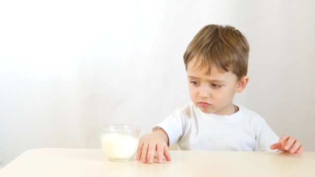 The child refuses to drink milk from a glass cup. Shooting on white background.