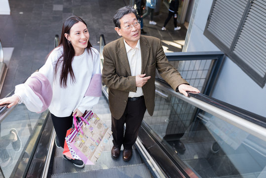Japanese Grandfather and granddaughter in the escalator of Barcelona Arena mall with bags shopping