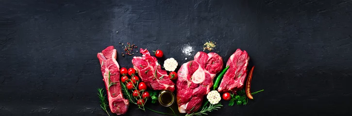 Papier Peint photo Viande Steak de viande fraîche crue avec tomates cerises, piment fort, ail, huile et herbes sur pierre sombre, fond de béton. Bannière.
