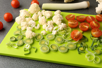 Cut leeks, cherry tomatoes and cauliflower on cutting board. Fresh vegetables sliced on bright green board.