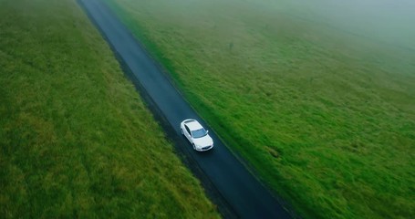 Cinematic aerial view of electric car driving on country road at sunset