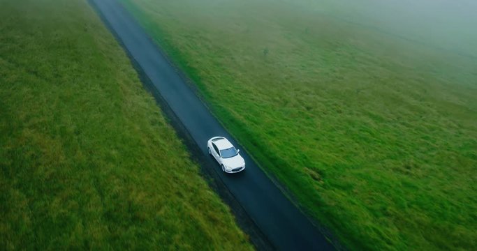 Cinematic aerial view of electric car driving on country road at sunset