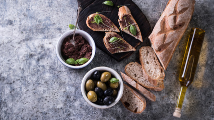 Green and black olives in tin cans ,fresh bread,bottle of olive oil on old wood background. italian food concept