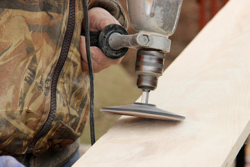 Process with angle grinder. Grinding of a wooden board 20 mm for the manufacture of furniture and shelves. An old man is working in the open air. Carpentry as a hobby. grinding wheel in daddy hand