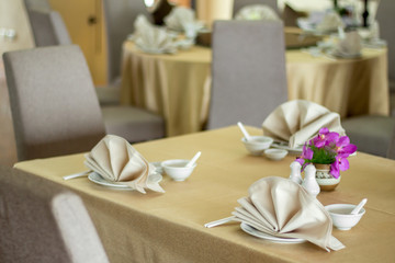 The table set in restaurant with the bowl spoon chopsticks and violet orchids on the table with the warm natural light in a day time to present the luxury setting in high class hotel or resort. 