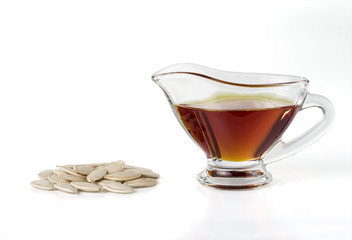 Pumpkin oil in a glass sauceboat and pumpkin seeds isolated on white background.