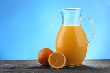 Jug of orange juice and oranges  on blue