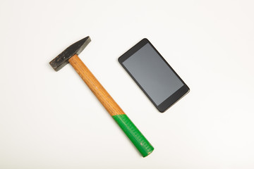 Close-up of a smartphone next to a hammer on white