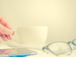 Serving a cup of coffee for relaxing time. Cross processed tone of woman hand, coffee cup, eyeglasses and mobile phone.