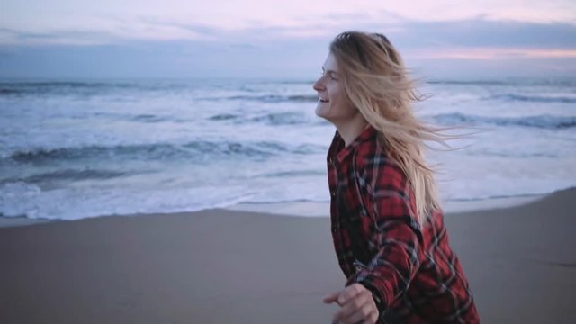 Slow motion video of young successful and beautiful woman running on beach at sunset, happy and excited celebrates winning or just life. Looks ahead into bright future, is proud independent, confident