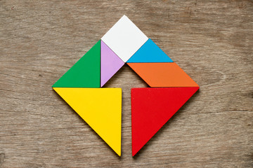 Colorful tangram puzzle in square with inside arrow direction shape on wood background