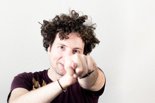 Portrait of a young, Caucasian, brunet, curly haired man showing fig gesture on white background.