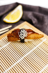 sushi with eel on a wooden rug with chopsticks and a slice of lemon