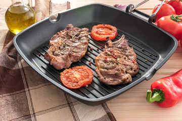 Grilled steak on grill pan with tomatoes on wooden background