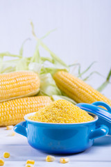 Corn grits polenta in a blue ceramic bowl on white table with ripe raw corn cob and green leaves