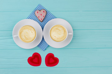 White cups with cappuccino and red hearts. Two porcelain cups with coffee drink, handmade hearts and heart shaped cookie. Valentines Day coffee composition.