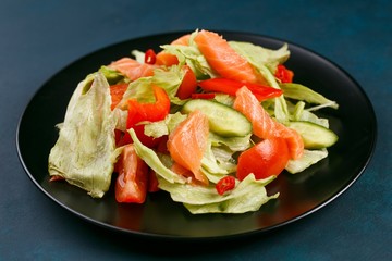 Delicious fresh vegetable salad with salmon on black plate, healthy food close up