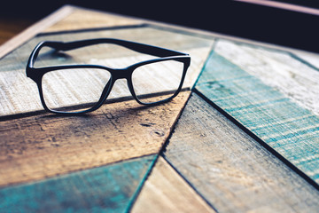 Modern black designer eyeglasses on weathered wood surface with angular pattern.