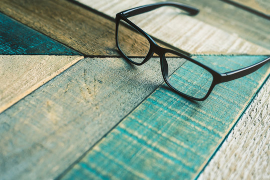 Modern black designer eyeglasses on weathered wood surface with angular pattern.