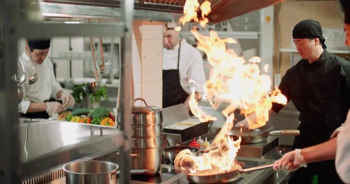 chef actively working in the kitchen of the restaurant with Asian cuisine, vegetables are roasted with fire,4K slow motion