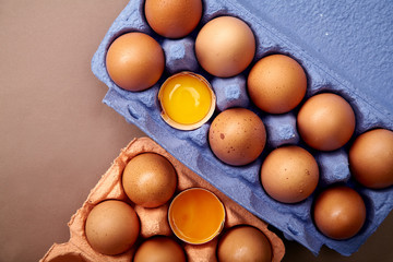 Horizontal closeup shot with two colorful cardboard containers of pink and violet color with chicken eggs, two egg yolks open and visible.
