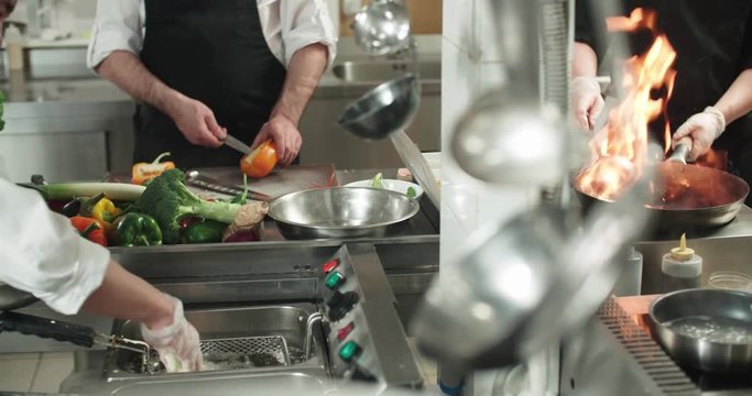 chef actively working in the kitchen of the restaurant with Asian cuisine, vegetables are roasted with fire,4K slow motion