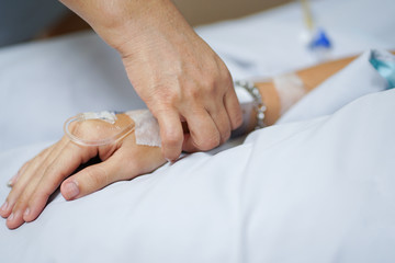 close up on patient hand laying on bed for check pulse or touch from his mother , take care concept