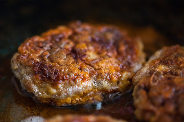 Steaks in a frying pan are roasted on the stove. Fried cutlets