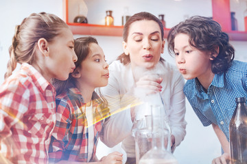 Work in team. Female chemistry teacher conducting a practical lesson with her pupils and involving them in the process of performing a chemical experiment.