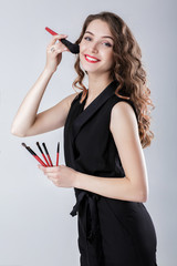 Naklejka premium woman make-up artist with natural make-up holding makeup brush on gray background