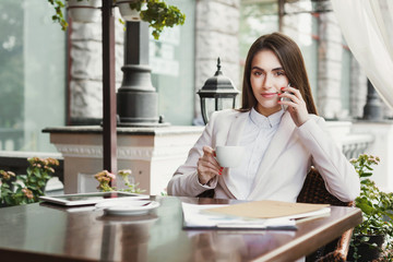 Young businesswoman talking on phone and drinking coffee outdoors
