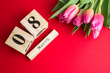 8 March Happy Women's Day concept. With wooden block calendar and pink tulips on red background