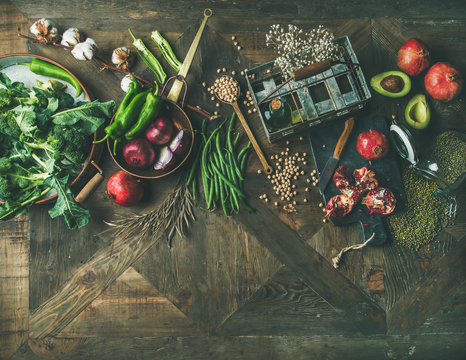 Winter vegetarian food cooking ingredients. Flat-lay of seasonal vegetables and fruit, beans, kitchen utencils over vintage wooden table background, top view, copy space. Healthy, clean eating concept