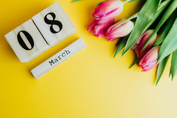 8 March Happy Women's Day concept. With wooden block calendar and pink tulips on yellow background
