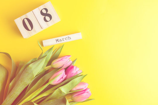 8 March Happy Women's Day concept. With wooden block calendar and pink tulips on yellow background