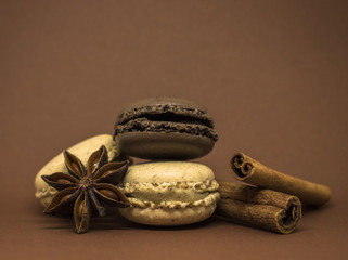 Vanilla and chocolate spicy macaroons with cinnamon sticks and anise on warm brown background. French sweets.