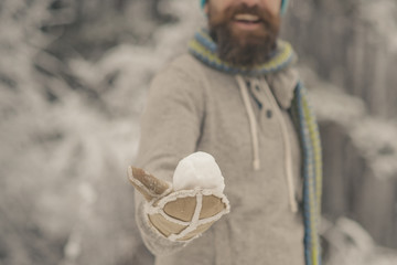 Hand with snowball in mitten of blurred bearded hipster