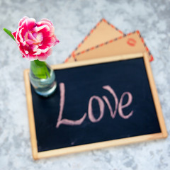 Obraz premium Pink tulip in glass bottle and vintage kraft envelopes with kiss print on background of black chalkboard with inscription love.