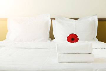 Stack of towels and flower on bed in hotel room