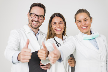 Portrait of three happy doctors who stand smiling and show thumbs up