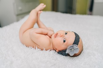 Cute three month old baby girl lying on th bed at home wearing beautiful head decoration