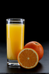 Glass of orange juice and oranges on black